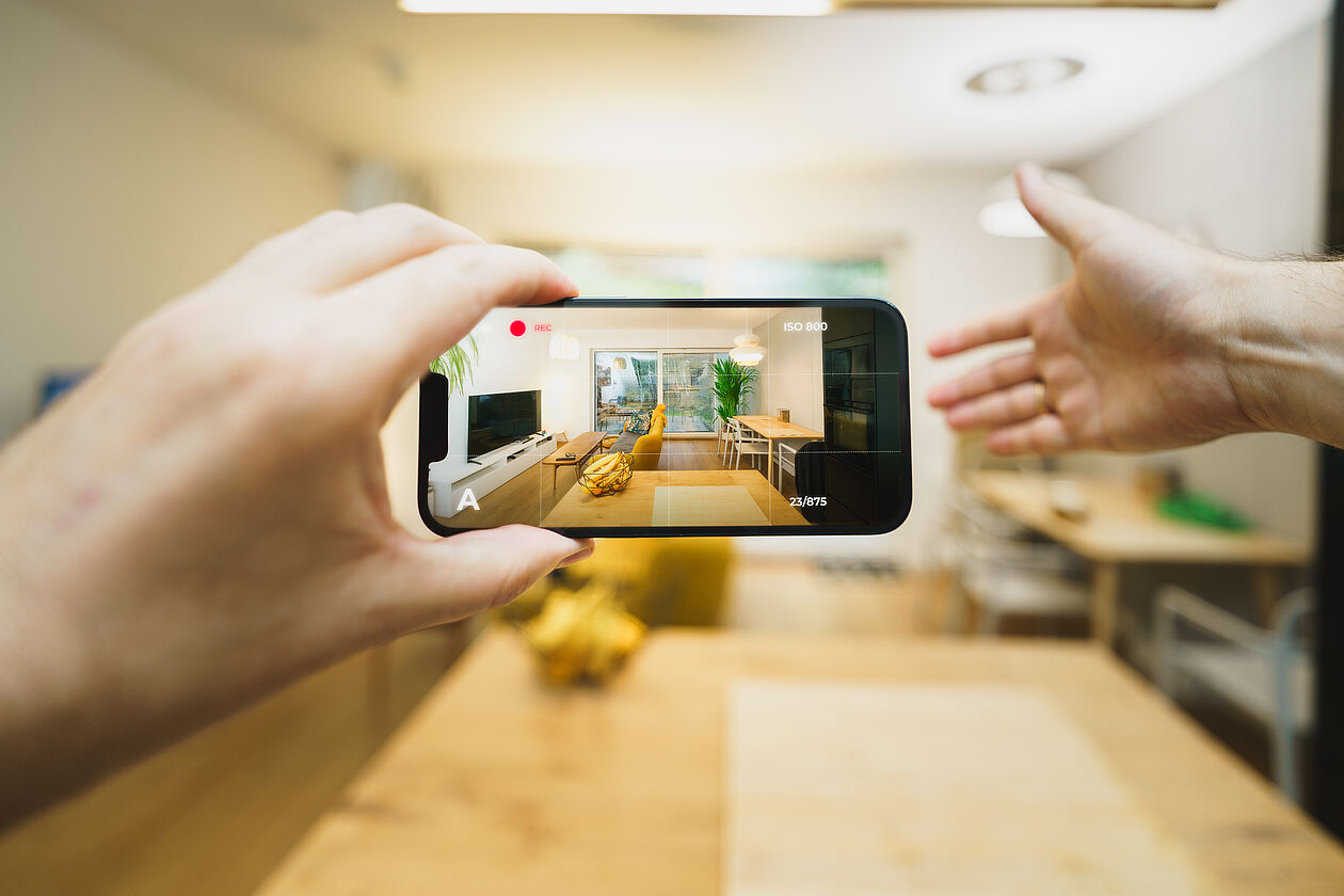 Eine Person filmt ein Wohnzimmer mit dem Smartphone für eine Online-Besichtigung.