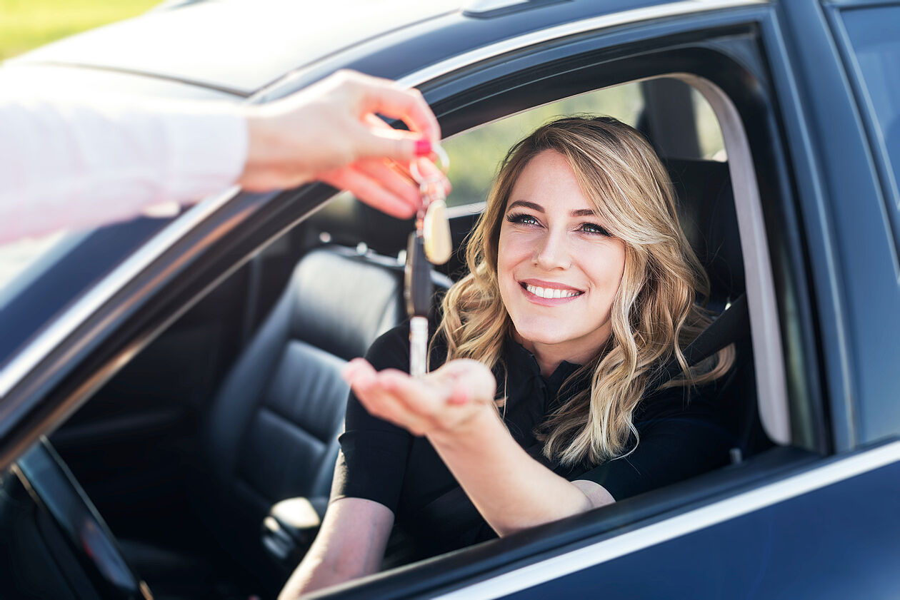 frau sitzt im auto und jemand reicht ihr den autoschlüssel