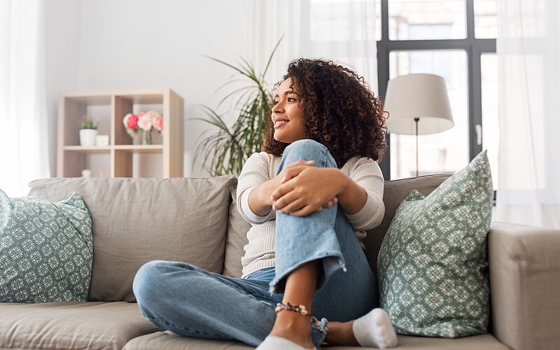Frau sitzt auf dem Sofa, möglicherweise zuhause,  und lächelt sympathisch.