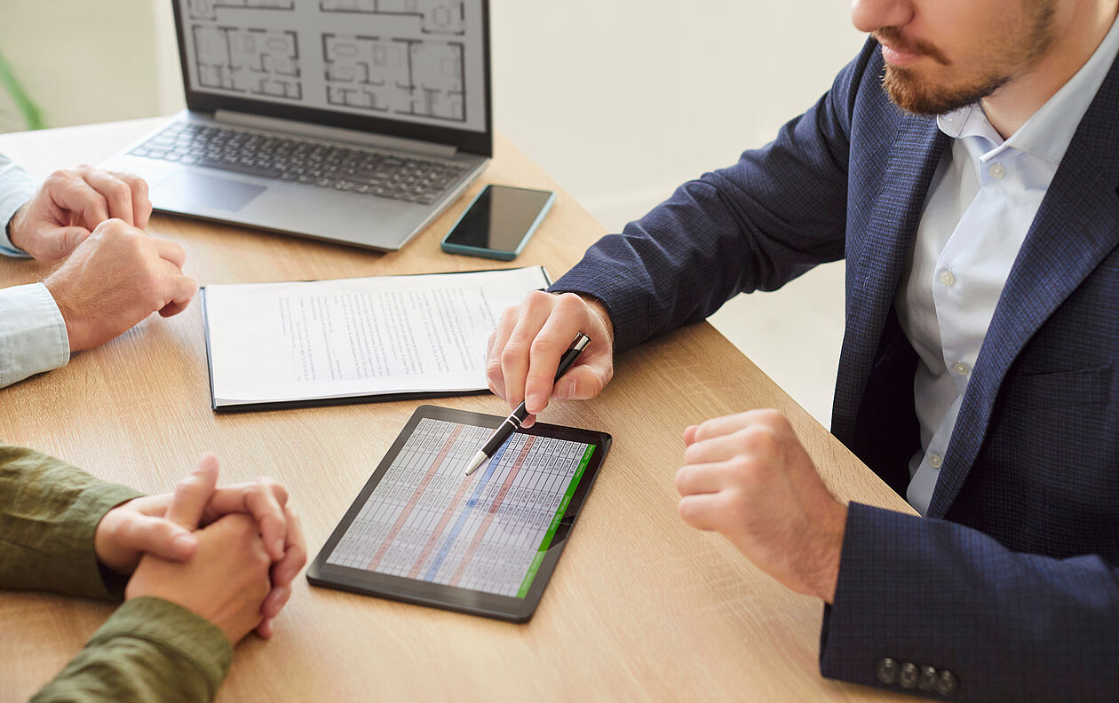 Ein Gutachter erklärt anhand von Dokumenten und einem Tablet die Berechnung der Restnutzungsdauer einer Immobilie.
