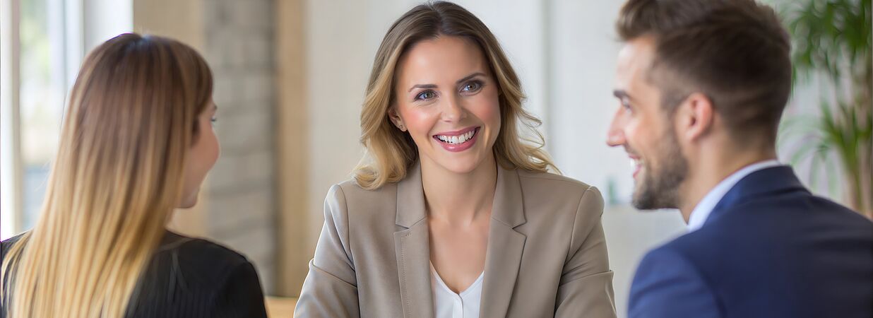 Frau berät lächelnd ein Paar in einem Gespräch über Kredite und Finanzierung.