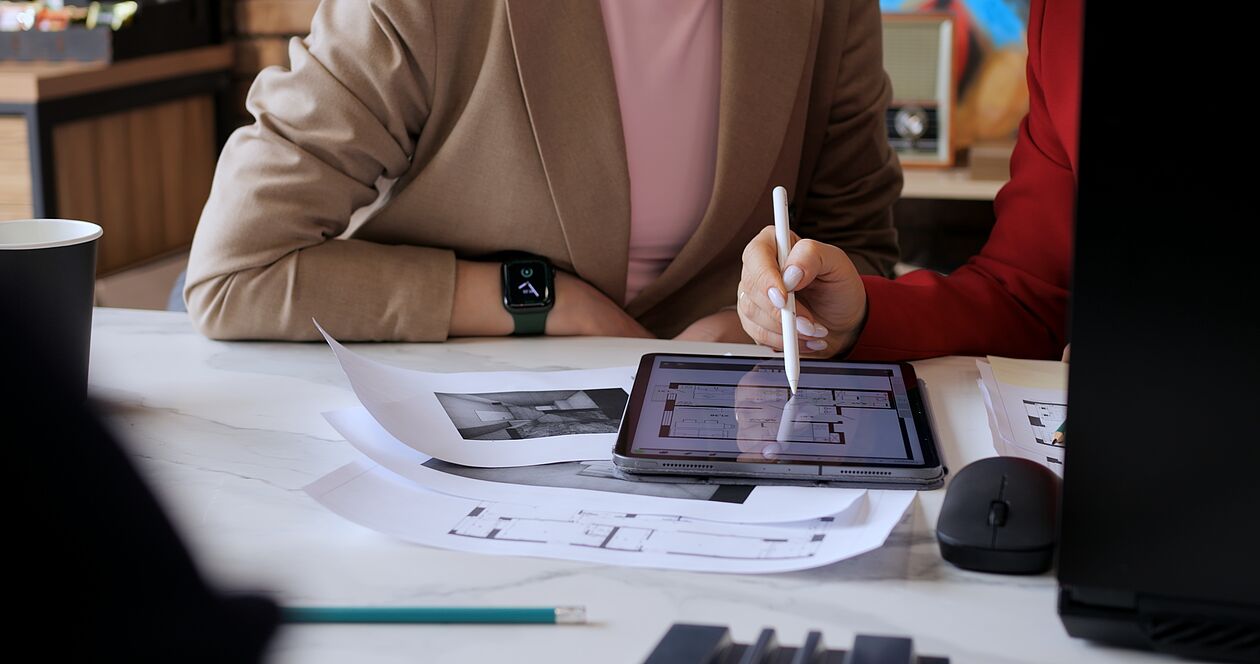 Zwei Personen planen Grundriss digital am Tablet mit ausgedruckten Bauzeichnungen