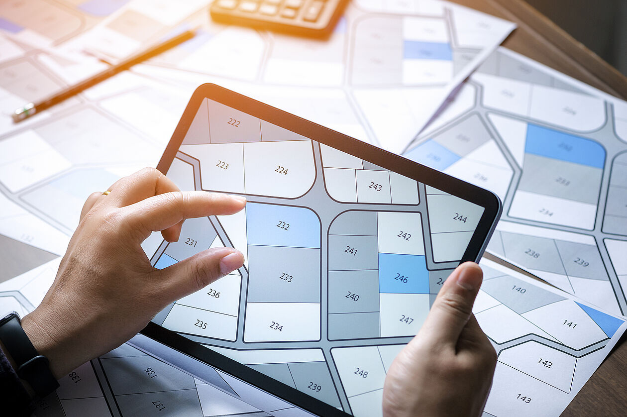 Eine Person betrachtet auf einem Tablet einen digitalen Parzellenplan mit Grundstücksgrenzen.