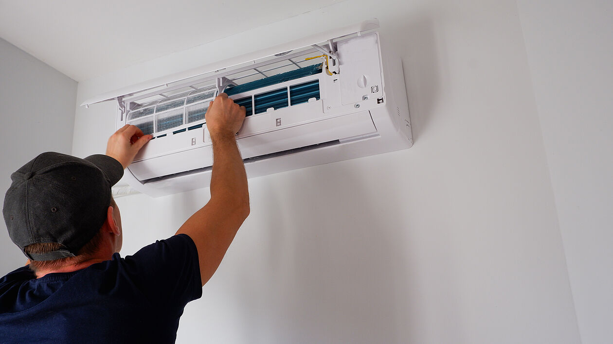 Handwerker montiert Split-Klimaanlage an Innenwand eines Hauses.
