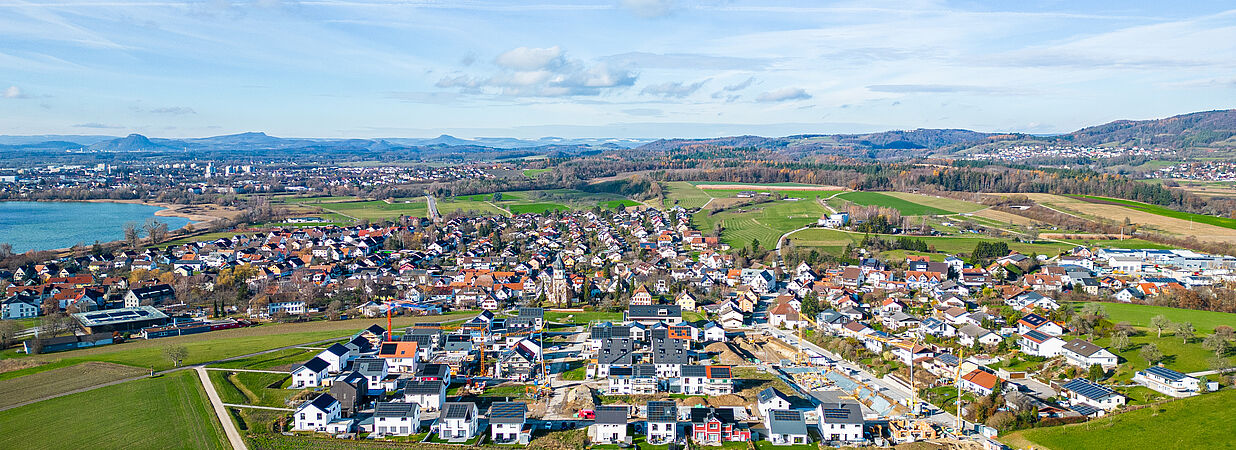 Luftaufnahme eines modernen Wohngebiets in ländlicher Umgebung mit Bergen im Hintergrund.