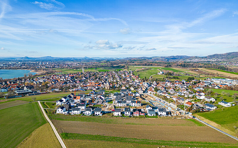 Luftaufnahme eines modernen Wohngebiets in ländlicher Umgebung mit Bergen im Hintergrund.