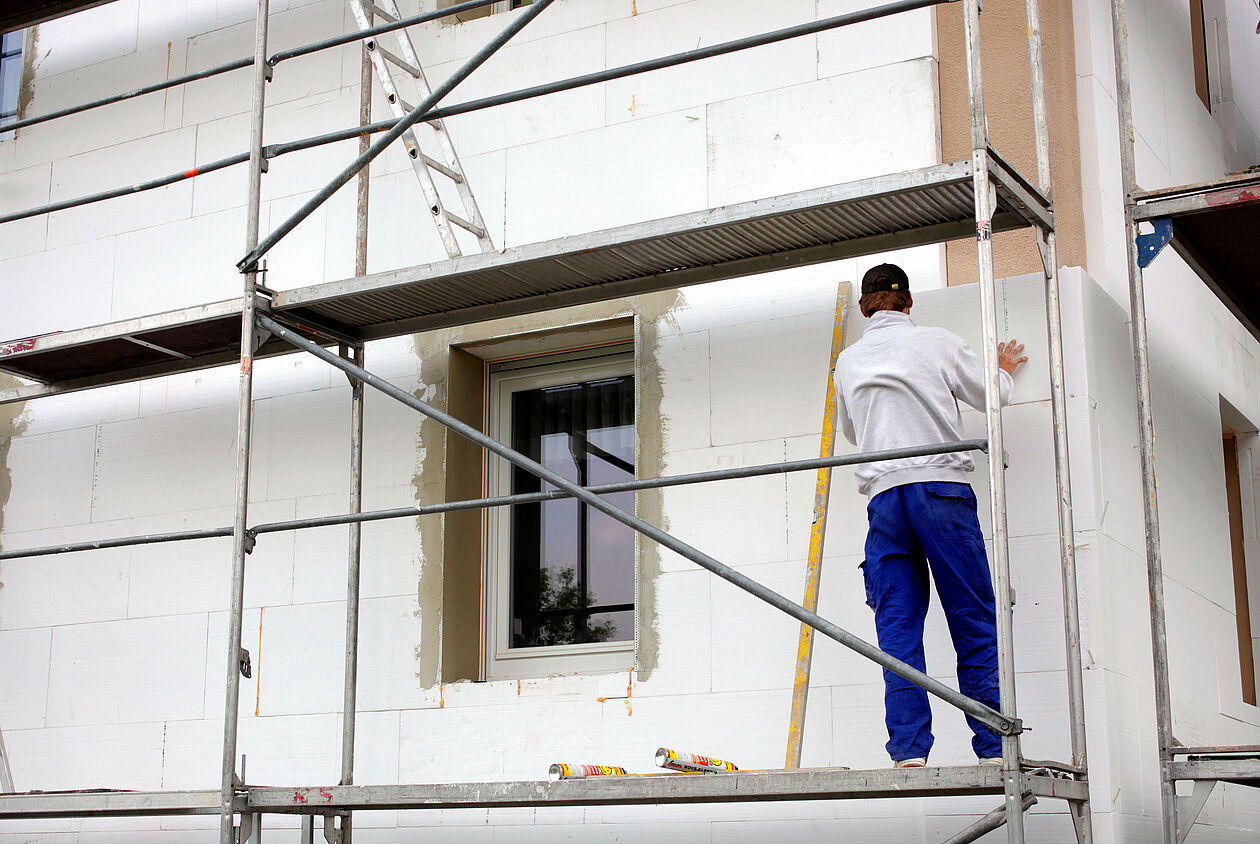 Handwerker bringt Dämmplatten an einer Hausfassade mit Gerüst an.