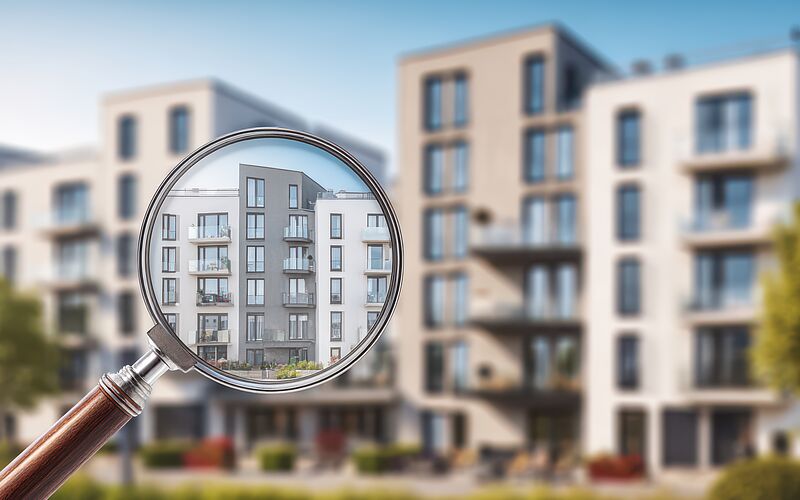 Mehrparteienhaus durch Lupe betrachtet – Symbol für Immobilienbewertung und Restnutzungsdauergutachten