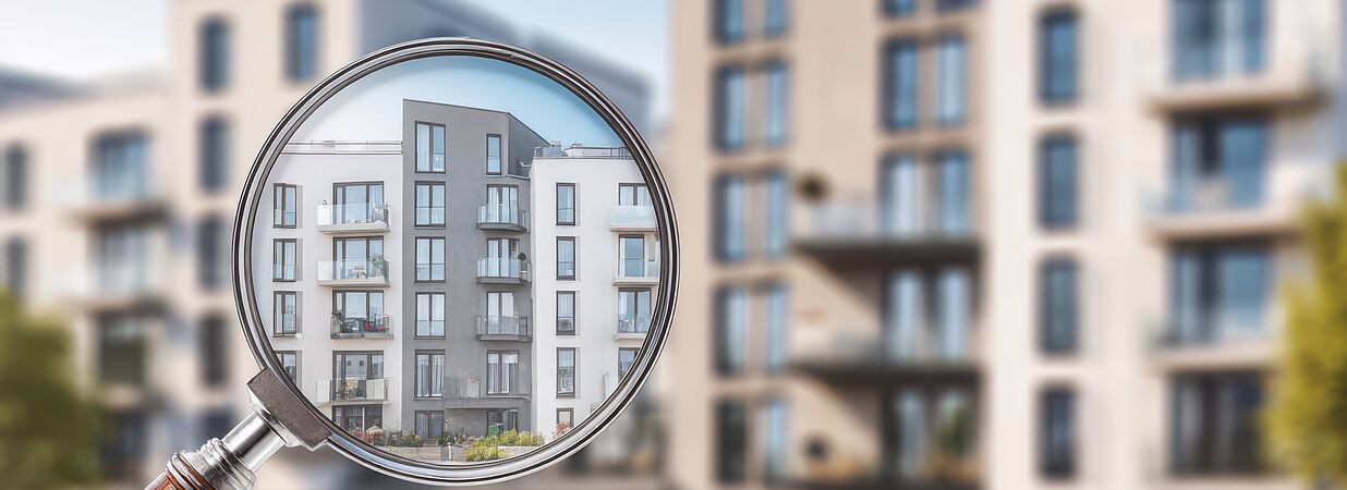 Mehrparteienhaus durch Lupe betrachtet – Symbol für Immobilienbewertung und Restnutzungsdauergutachten