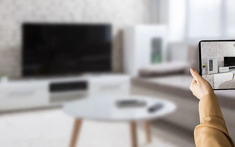 Eine Person betrachtet ein Wohnzimmer auf einem Tablet während einer virtuellen Immobilienbesichtigung.