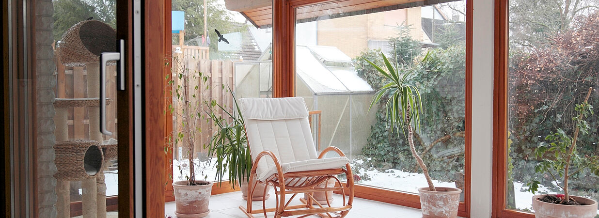 Moderner Wintergarten mit gemütlichem Sessel und Pflanzen, Ausblick auf verschneiten Garten – Beispiel für Wohnraumerweiterung.