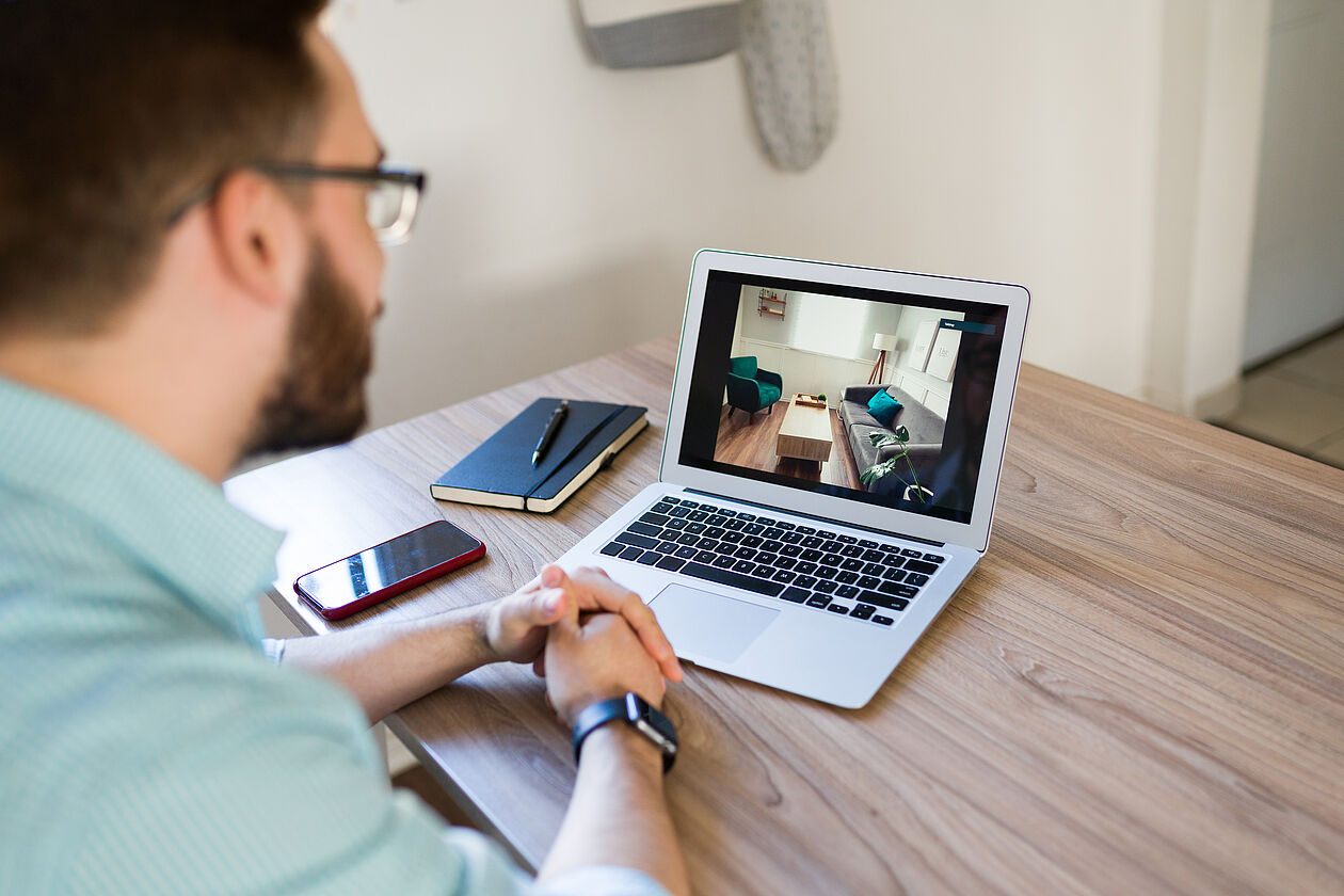 Ein Mann betrachtet eine Wohnung am Laptop für eine digitale Immobilienbesichtigung.