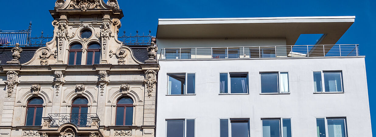Vergleich eines historischen Altbaus und eines modernen Neubaus bei strahlendem Himmel.