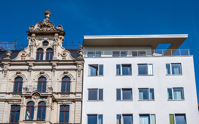 Vergleich eines historischen Altbaus und eines modernen Neubaus bei strahlendem Himmel.