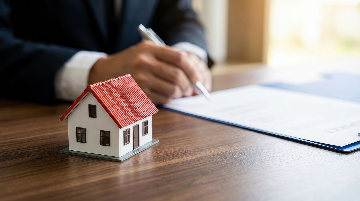 Hausmodell steht auf Tisch neben Vertrag und unterschreibender Person.