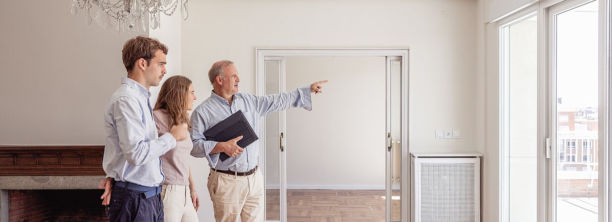 Ein Immobilienmakler zeigt einem Paar eine helle Wohnung während einer Besichtigung.