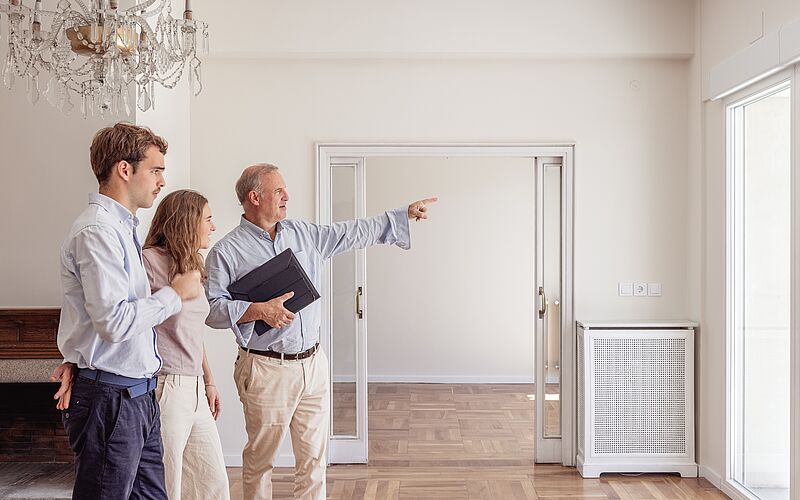 Ein Immobilienmakler zeigt einem Paar eine helle Wohnung während einer Besichtigung.