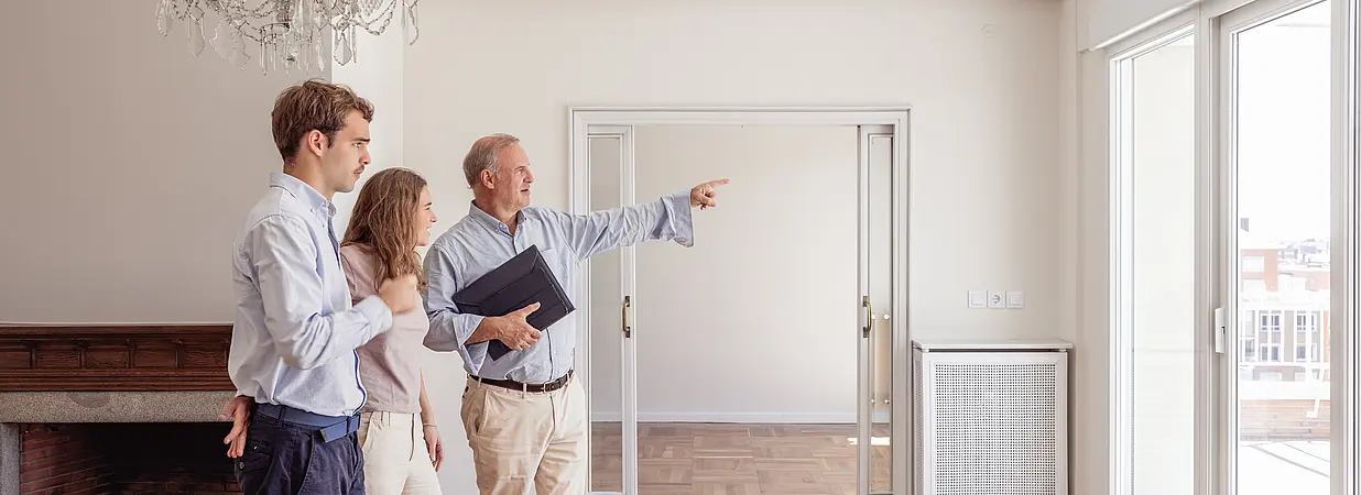 Ein Immobilienmakler zeigt einem Paar eine helle Wohnung während einer Besichtigung.