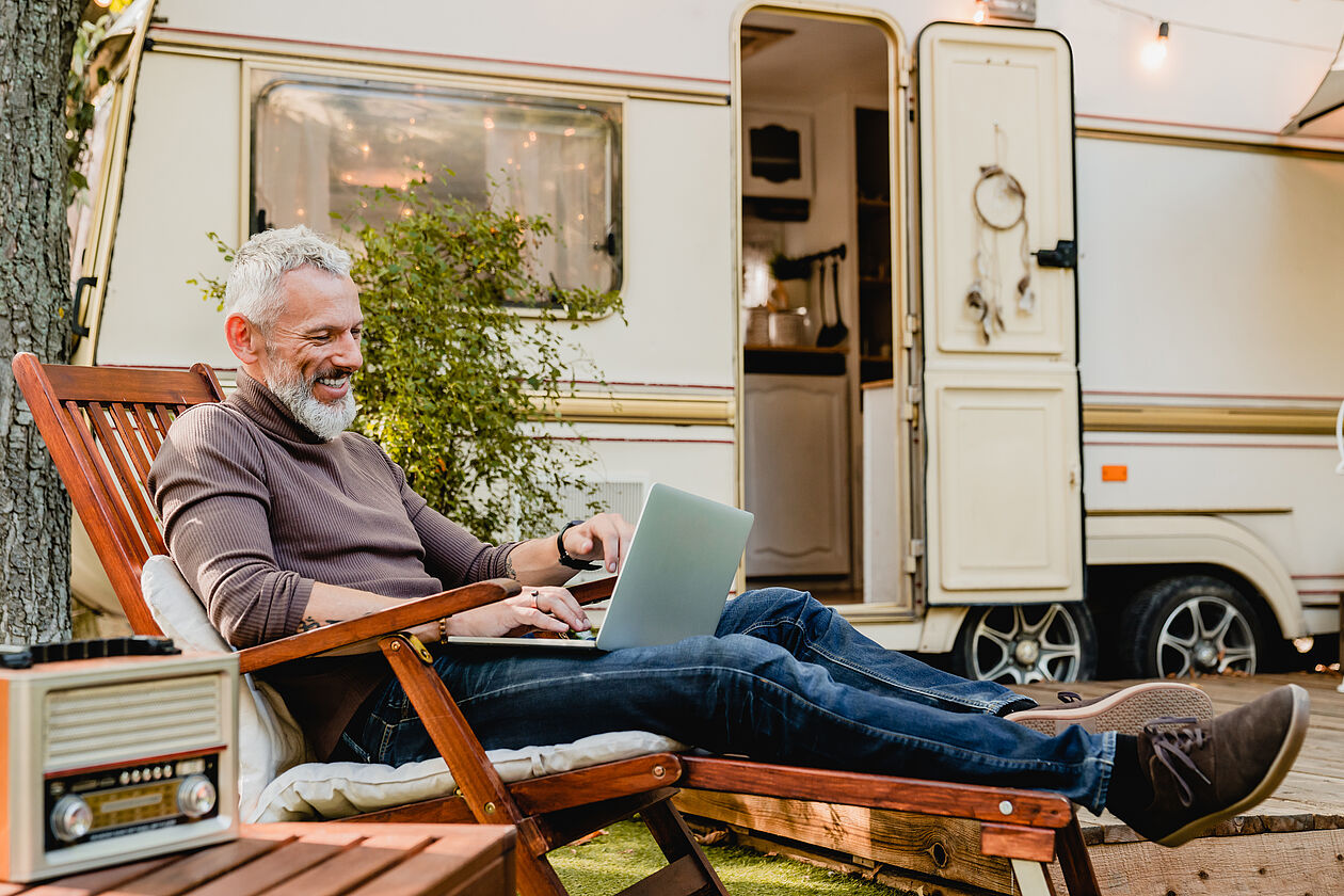 Mann sitzt mit Laptop vor Wohnmobil