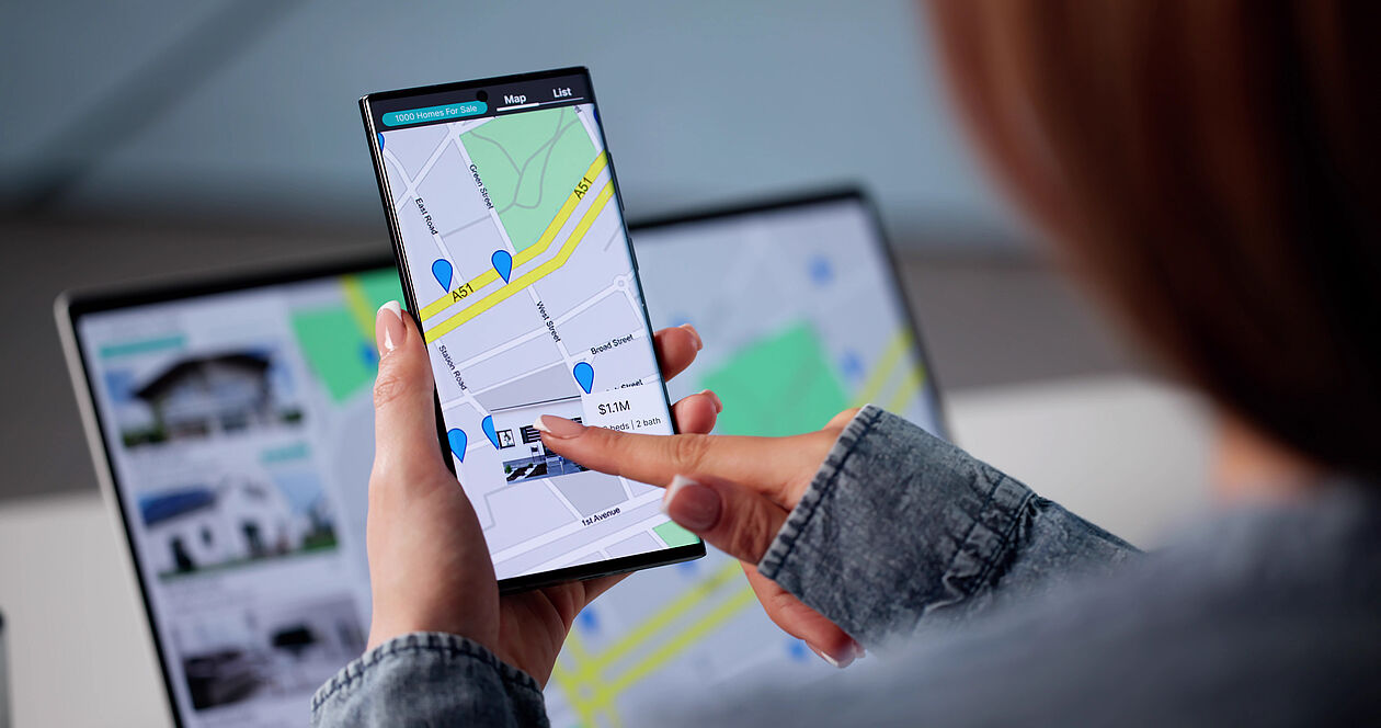 Person sucht mit Smartphone und Karte nach Mietwohnungen in passender Lage.