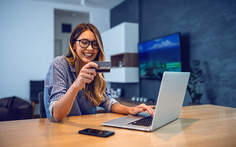frau sitzt am laptop und hält kreditkarte in der hand