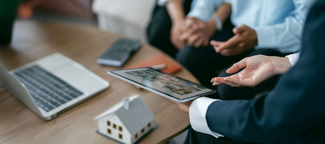 Finanzberater erklärt einem Paar eine Immobilienfinanzierung am Tablet.