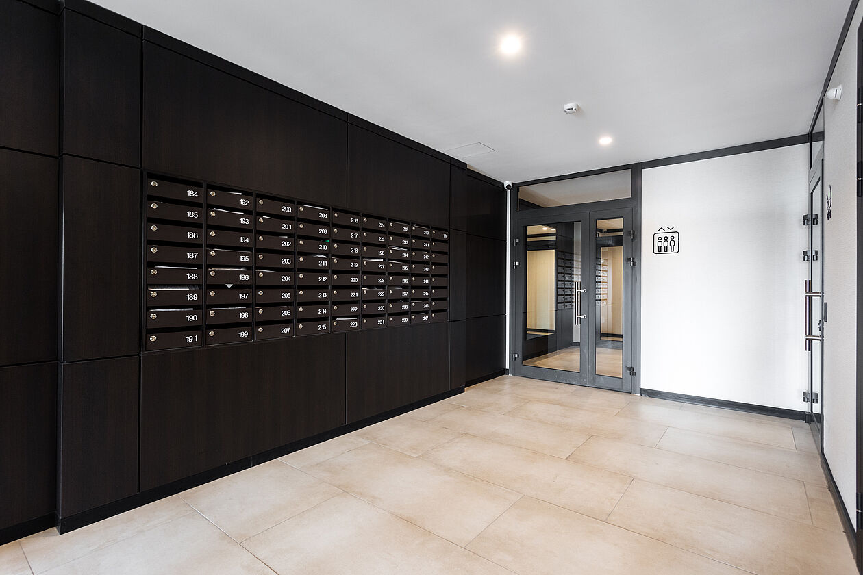 Eingangsbereich eines Mehrfamilienhauses mit Briefkästen und Zugangstür.