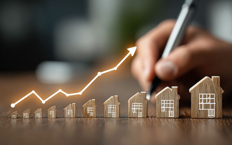 Steigende Zinsen bei Immobilienfinanzierungen symbolisiert durch Hausmodelle und Wachstumskurve