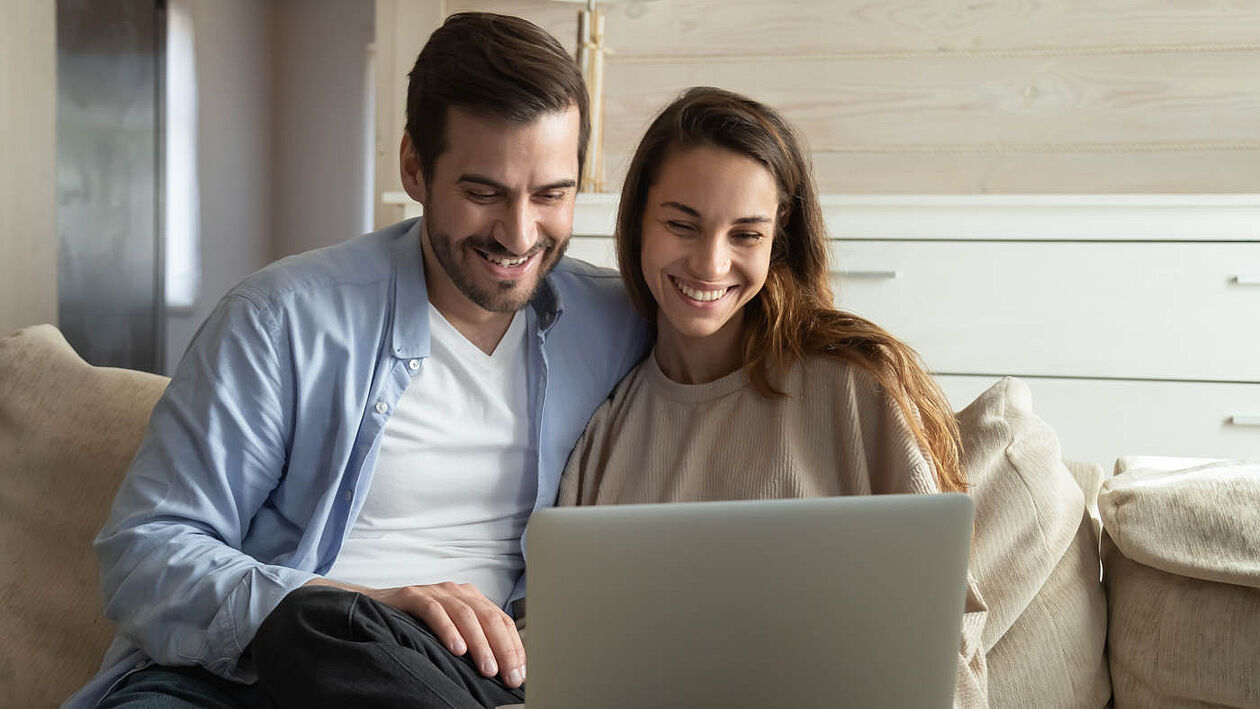 glückliches paar sitzt mit laptop auf der couch