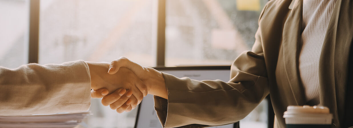 Zwei Personen in Business-Kleidung geben sich im Büro die Hand nach Vertragsabschluss.