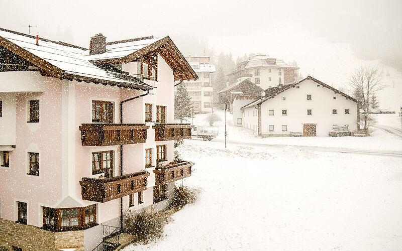 Mehrfamilienhaus im Schneefall – winterliche Szenerie in den Alpen mit umliegenden Gebäuden.