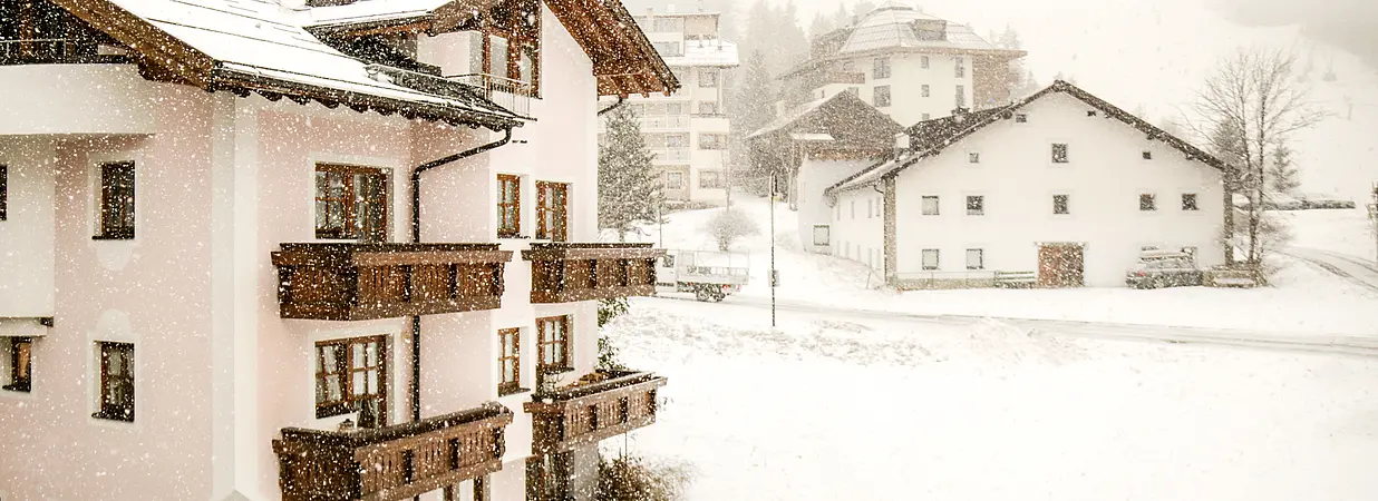 Mehrfamilienhaus im Schneefall – winterliche Szenerie in den Alpen mit umliegenden Gebäuden.