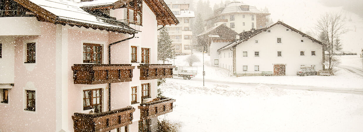 Mehrfamilienhaus im Schneefall – winterliche Szenerie in den Alpen mit umliegenden Gebäuden.