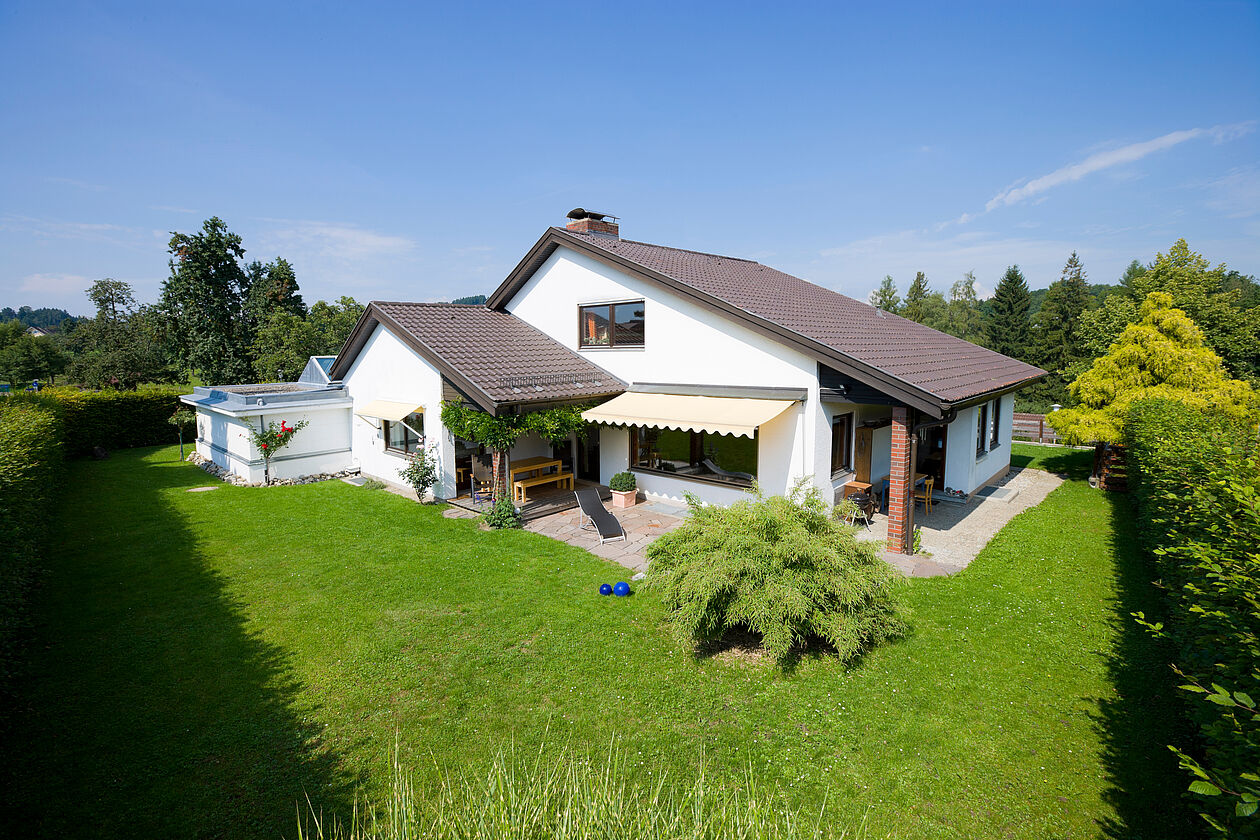 Ein Einfamilienhaus mit Schrägdach und Garten in der Sonne. 