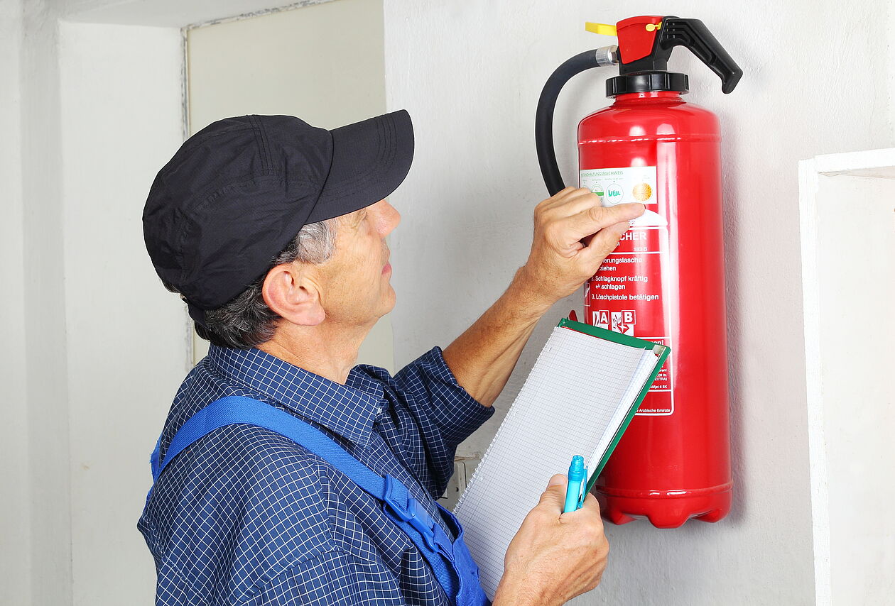 Ein Fachmann führt die Prüfung eines Feuerlöschers durch. Er sieht sich die Etiketten auf dem Gerät an.