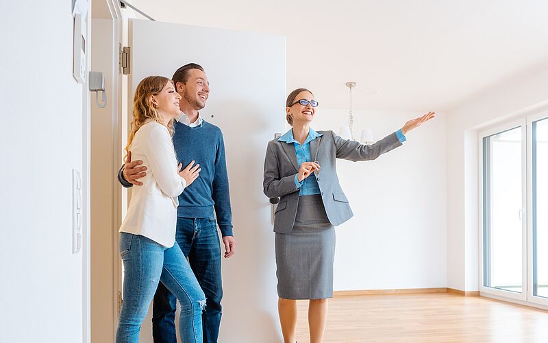 Frau zeigt einem Paar eine leere Wohnung. 