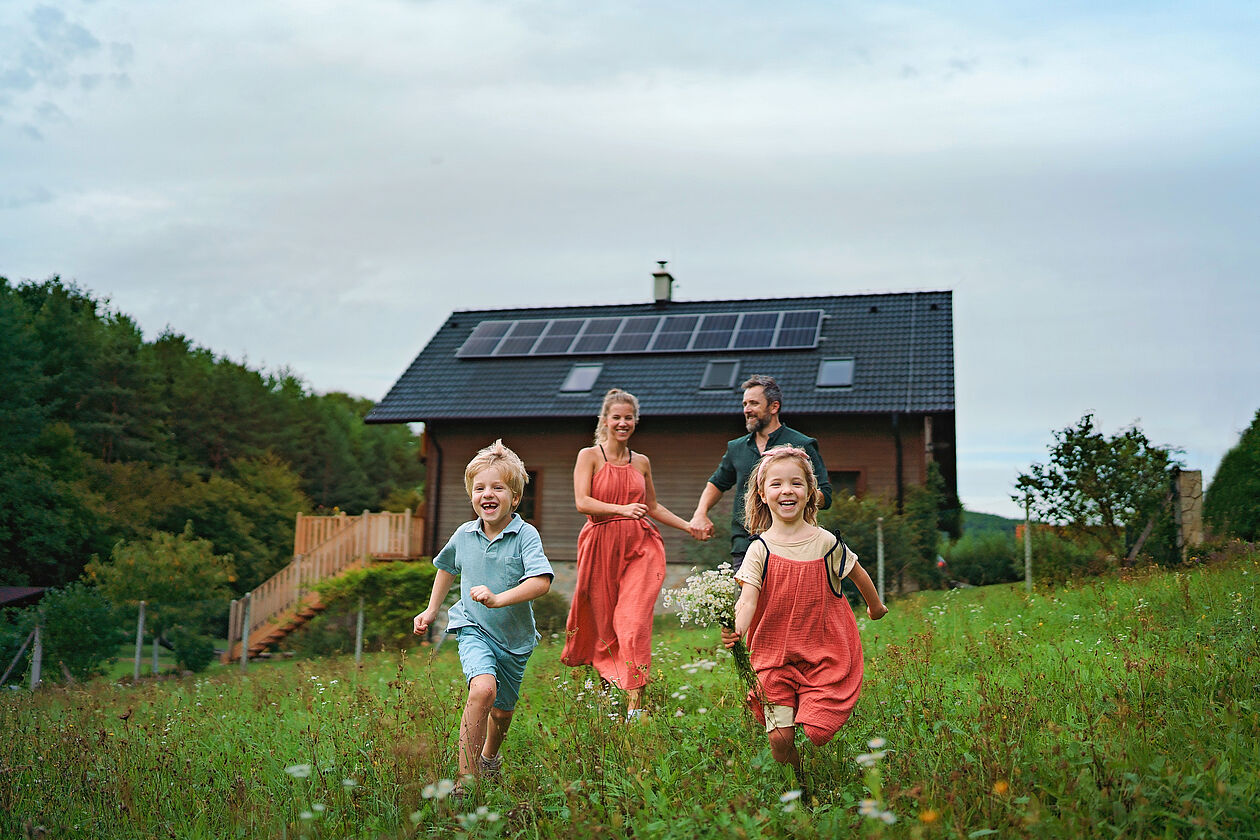 lachende familie rennt vor haus mit pv-anlage