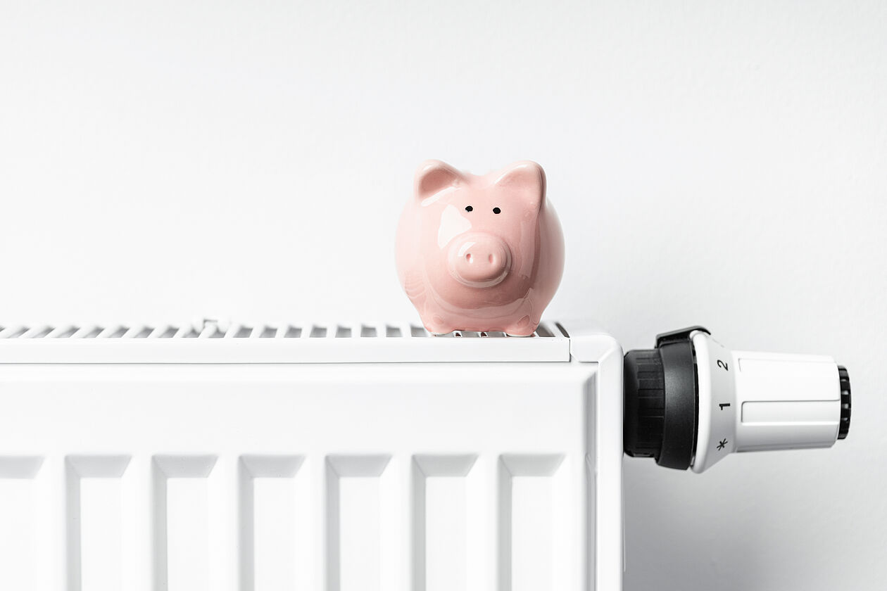 Sparschwein steht auf Heizkörper mit Thermostat