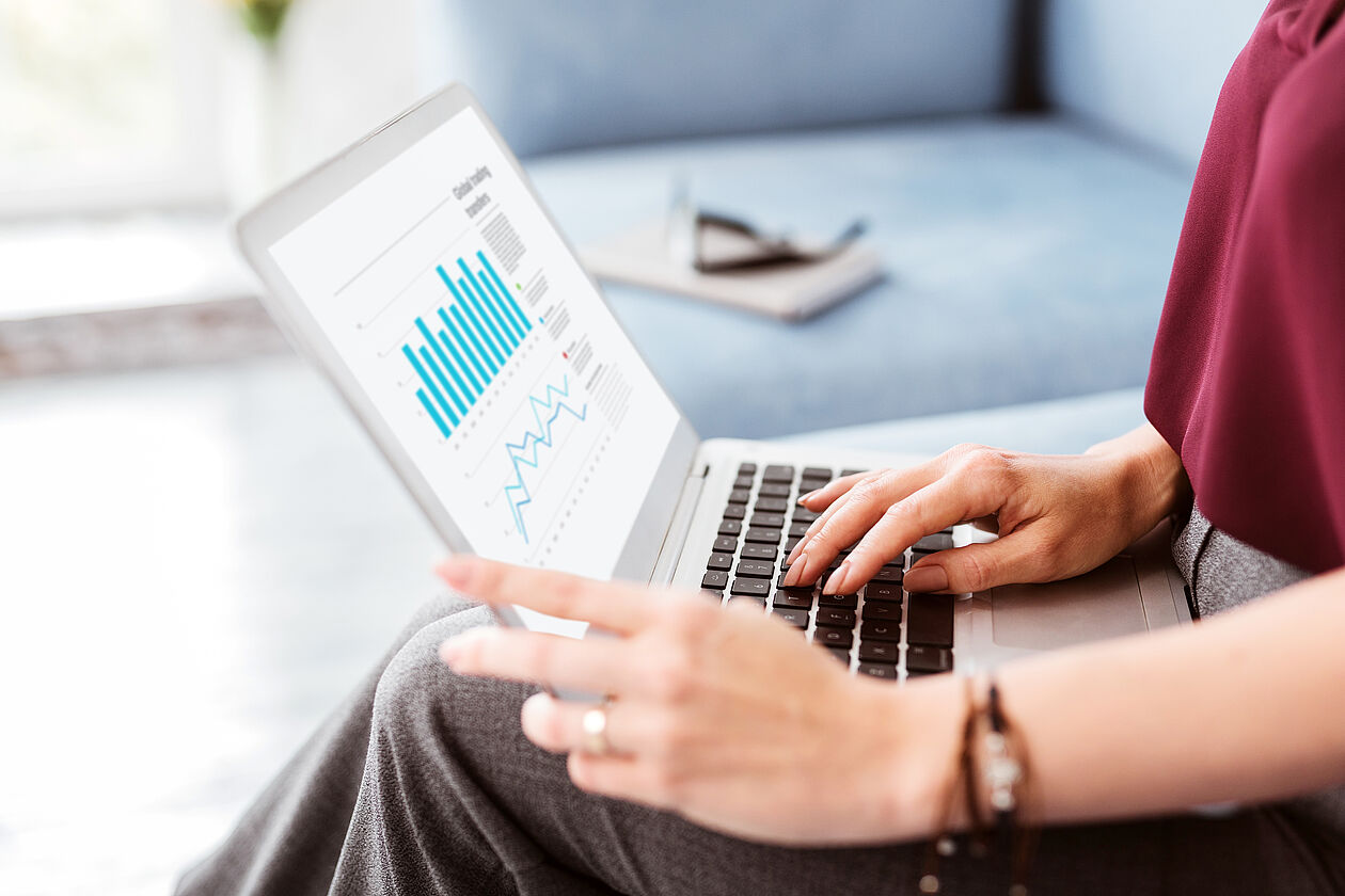 Person analysiert Zinsentwicklung und Finanzdiagramme auf Laptop zur Kreditplanung