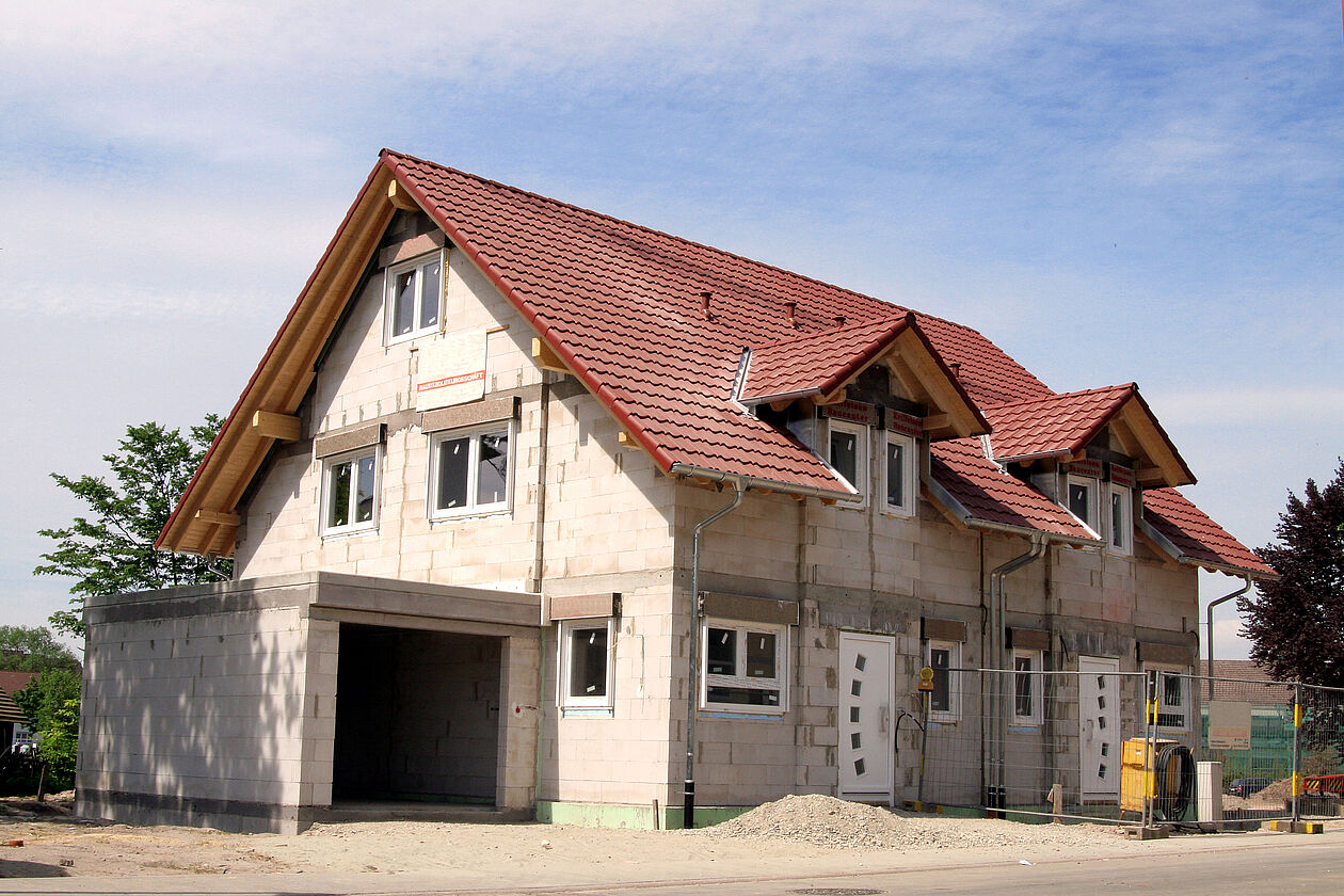 Ein Neubau eines Doppelhauses mit Garage steht in der Sonne.