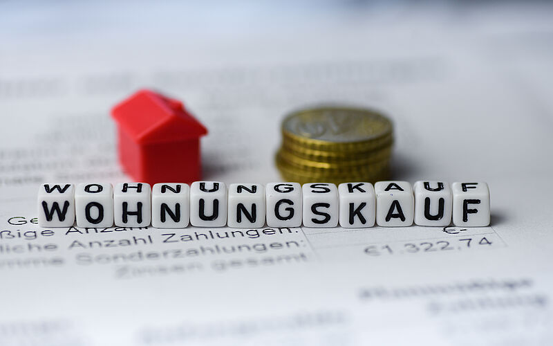 Buchstabenwürfel mit Miniaturhaus und Geldmünzen