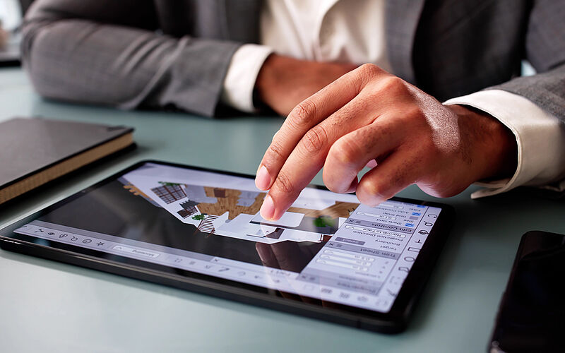 Architekt zeigt digitalen Haus-Grundriss auf Tablet in moderner Büro-Umgebung.