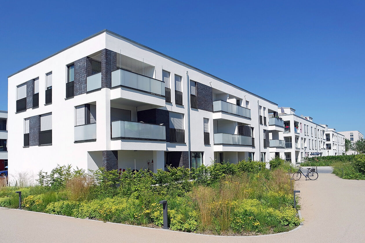 Moderne Neubau-Wohnanlage mit Balkonen, großen Fenstern und begrünter Umgebung an einem Sommertag.