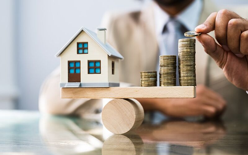 haus und münzen auf einer waage