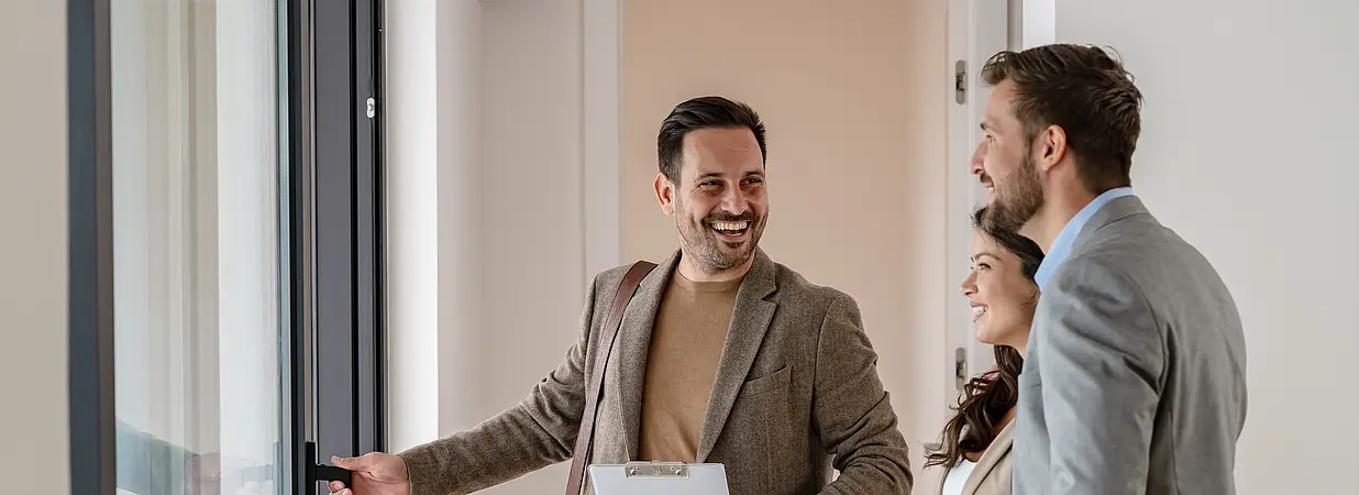 Immobilienmakler zeigt einem Paar eine Wohnung bei einer Besichtigung.