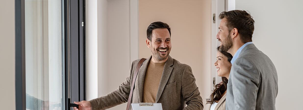 Immobilienmakler zeigt einem Paar eine Wohnung bei einer Besichtigung.