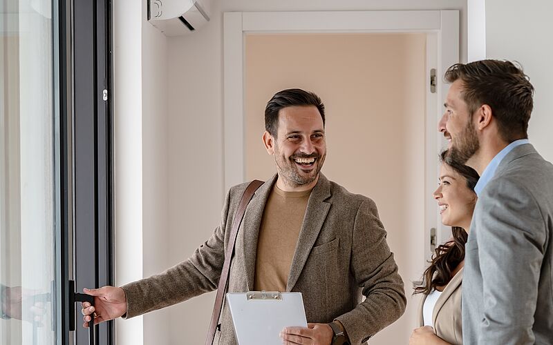 Immobilienmakler zeigt einem Paar eine Wohnung bei einer Besichtigung.