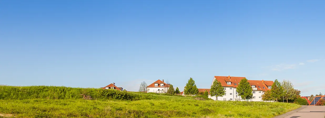 Neubaugebiet mit grüner Wiese, Straße und Einfamilienhäusern unter klarem, blauem Himmel.
