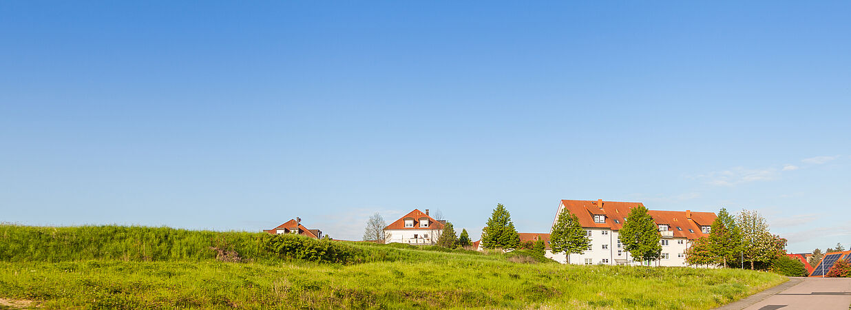 Neubaugebiet mit grüner Wiese, Straße und Einfamilienhäusern unter klarem, blauem Himmel.