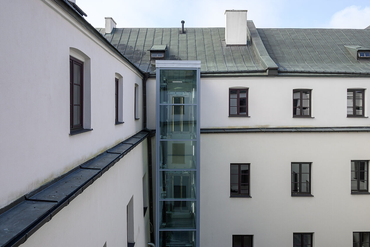 Ein moderner Glas-Außenaufzug, der an der Fassade eines mehrstöckigen Wohnhauses nachgerüstet wurde.